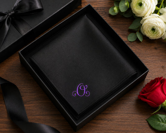 Black box with a purple monogram on a wooden surface with flowers.