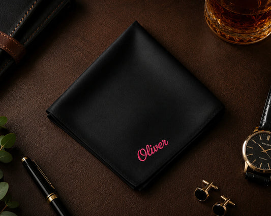 Black cotton hanky with 'Oliver' embroidery on a dark surface with accessories.