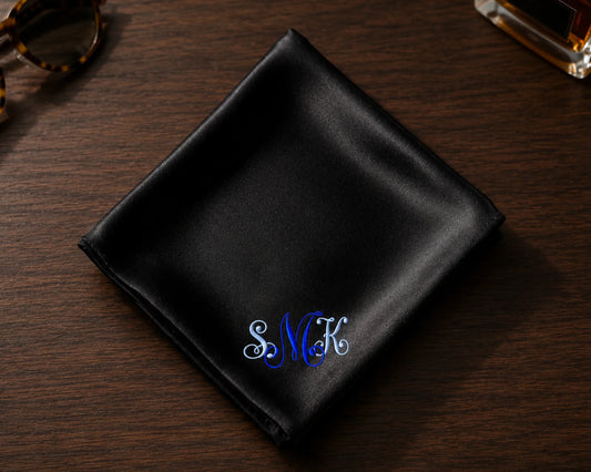 Black satin pocket square with embroidered initials on a wooden surface