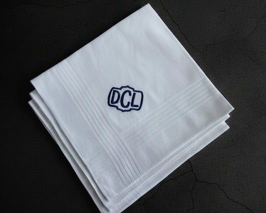 Three white cotton men's handkerchiefs featuring a navy blue embroidered shield monogram DCL on a dark background
