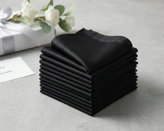 Stack of black folded handkerchief on a light gray surface with white flowers in the background.