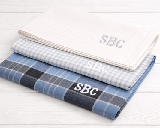 Two folded fabrics with 'SBC' monogram on a white wooden surface