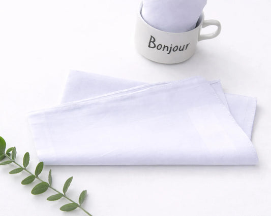 White hanky with 'Bonjour' text and folded white napkin on a light surface.