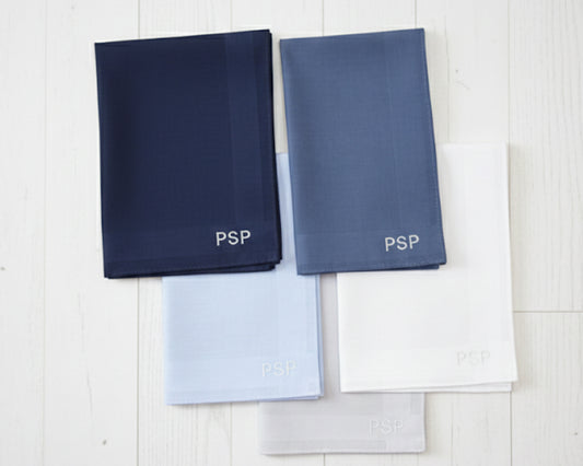 A set of four folded cotton handkerchiefs in navy blue and light grey featuring custom gold block ABC monograms.