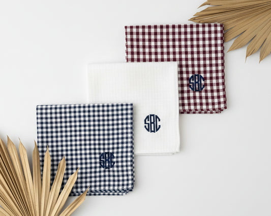 Five rolled cotton pocket squares in various gingham colors featuring custom initials next to a white coffee mug.