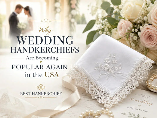 White embroidered wedding handkerchief with floral lace trim displayed beside bridal flowers, pearls, and wedding stationery in a soft romantic luxury setting