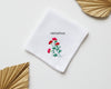Pure white cotton handkerchief featuring a centered red carnation embroidery with green stems on a neutral background