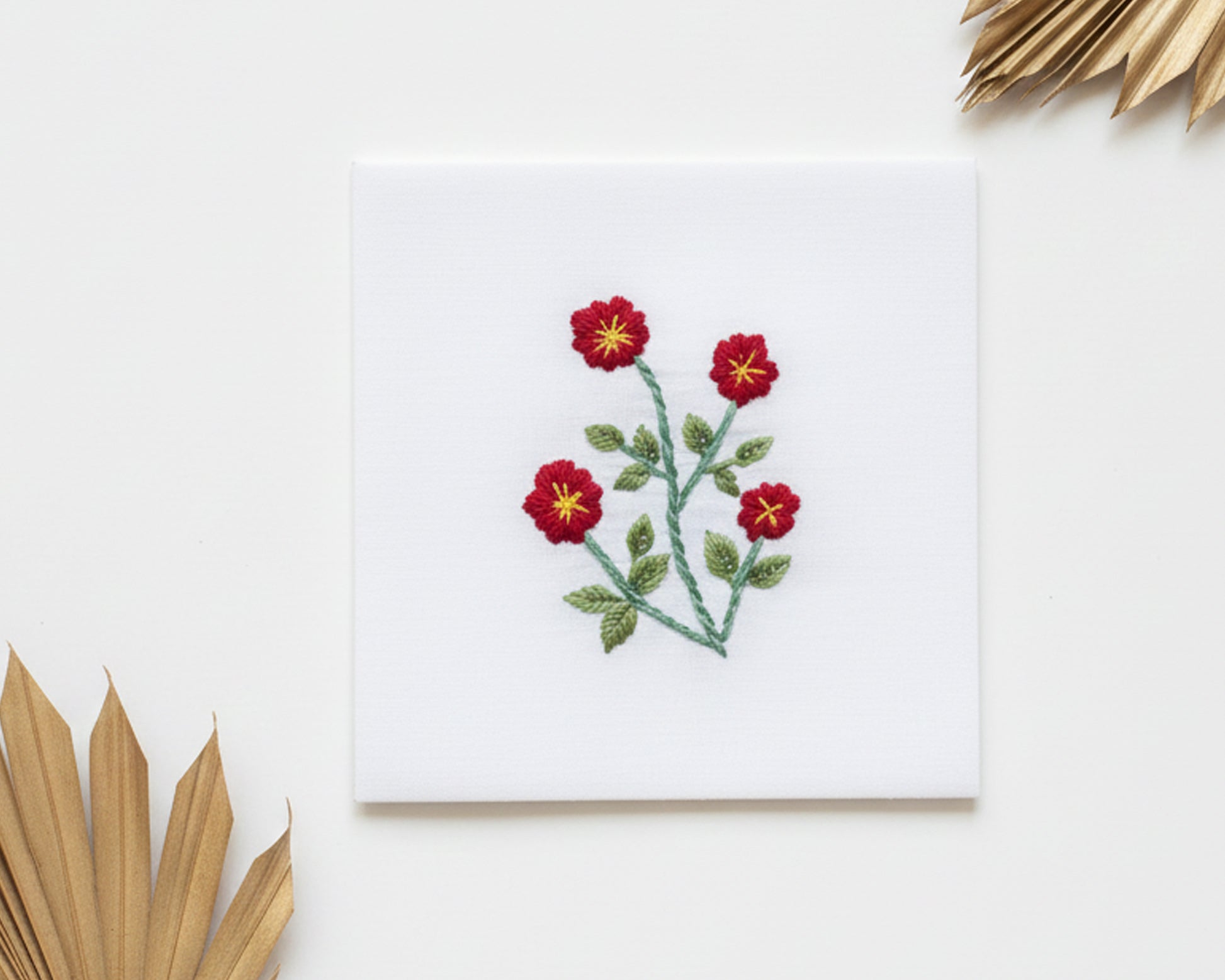 Pure white cotton handkerchief featuring centered red floral embroidery with gold centers on a neutral background