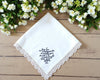 Personalized white cotton wedding handkerchief featuring detailed floral lace edging and a custom 2023 date on a white brick background