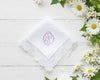 White cotton women's handkerchief with a blue baroque initial embroidery and scalloped edges near white flowers
