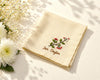 Beige hanky with embroidered design and text on a light surface with flowers.