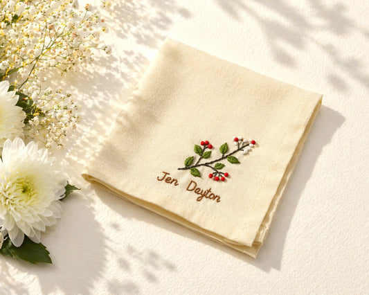 Beige hanky with embroidered design and text on a light surface with flowers.