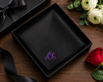 Black box with a purple monogram on a wooden surface with flowers.