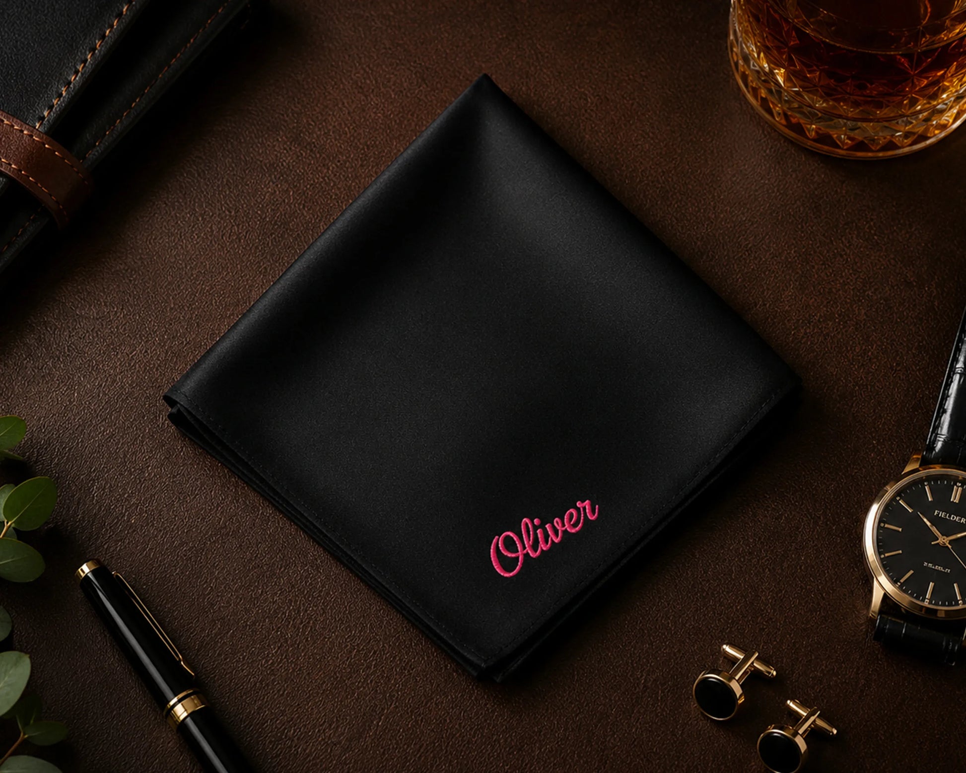 Black cotton hanky with 'Oliver' embroidery on a dark surface with accessories.