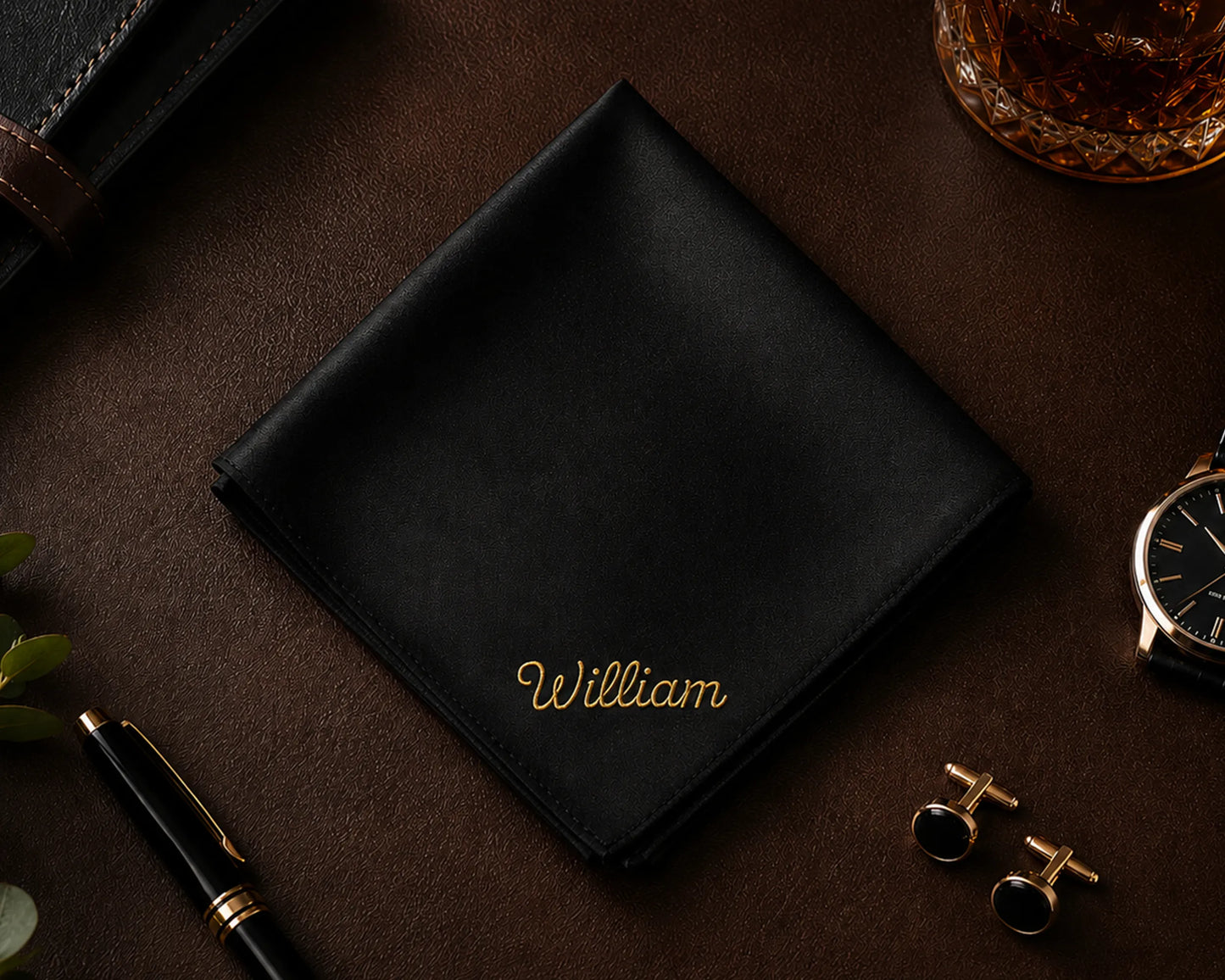 Black cotton hanky with 'William' embroidery on a dark surface with accessories.
