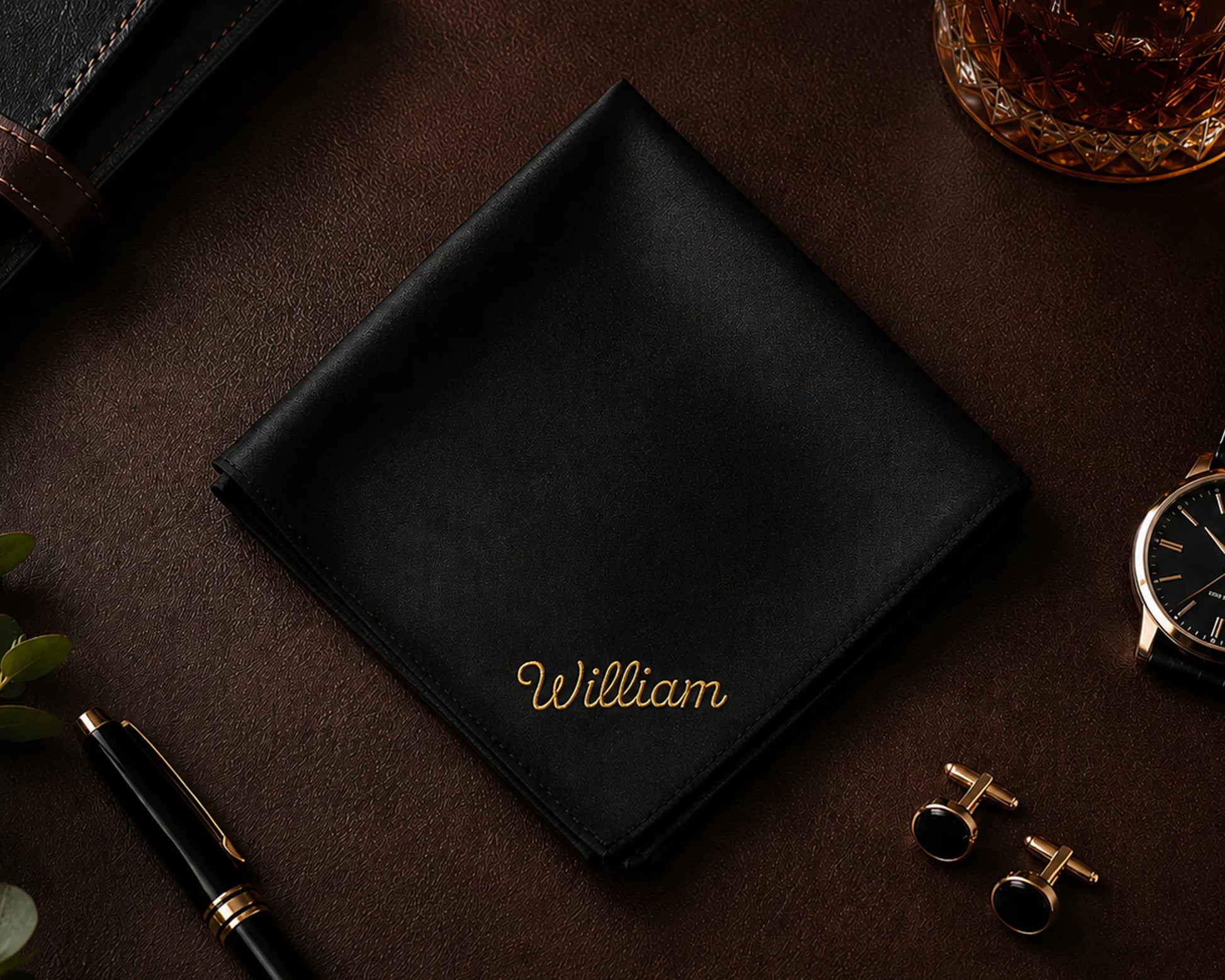 Black cotton hanky with 'William' embroidery on a dark surface with accessories.