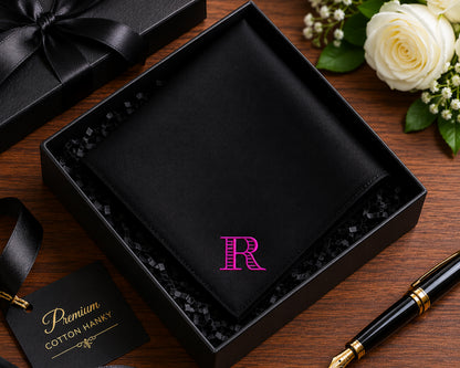 Black hankie with pink 'R' in a box on a wooden surface with flowers and a pen.