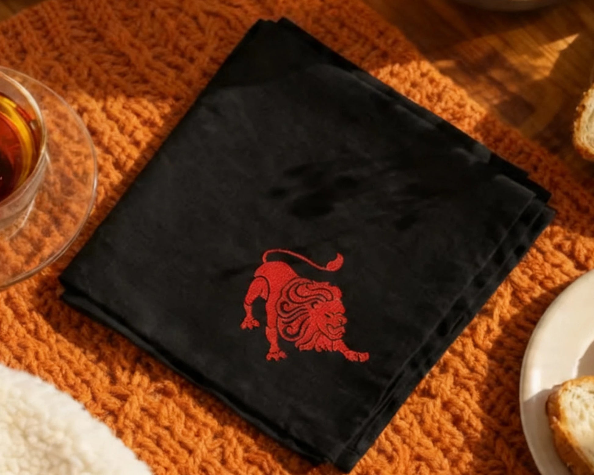 Black hanky with a red lion emblem on an orange textured surface.