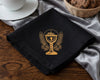 Black hanky with gold emblem on a wooden table with a basket of cookies and a cup.