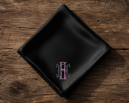 Black satin pocket square with a pink monogram on a wooden surface