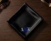 Black satin pocket square with embroidered initials on a wooden surface