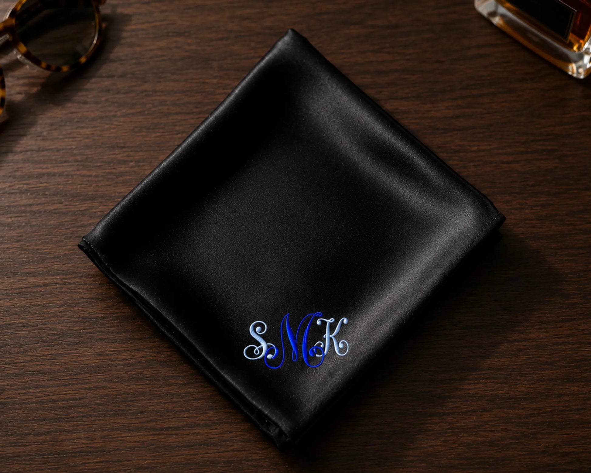 Black satin pocket square with embroidered initials on a wooden surface