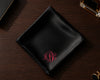 Black satin pocket square with red monogram on a wooden surface