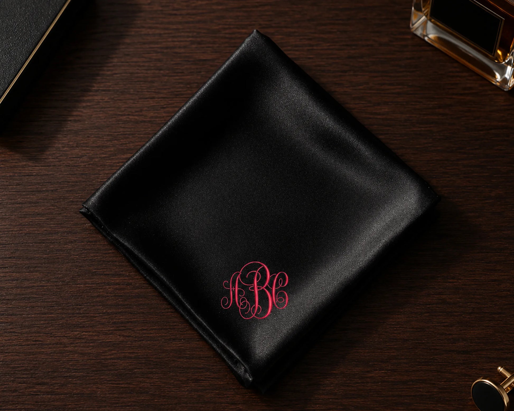 Black satin pocket square with red monogram on a wooden surface