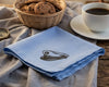 Blue hanky with embroidered designs on a wooden table with a cup and saucer.