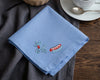 Blue hanky with embroidered designs on a wooden table with a cup and saucer.