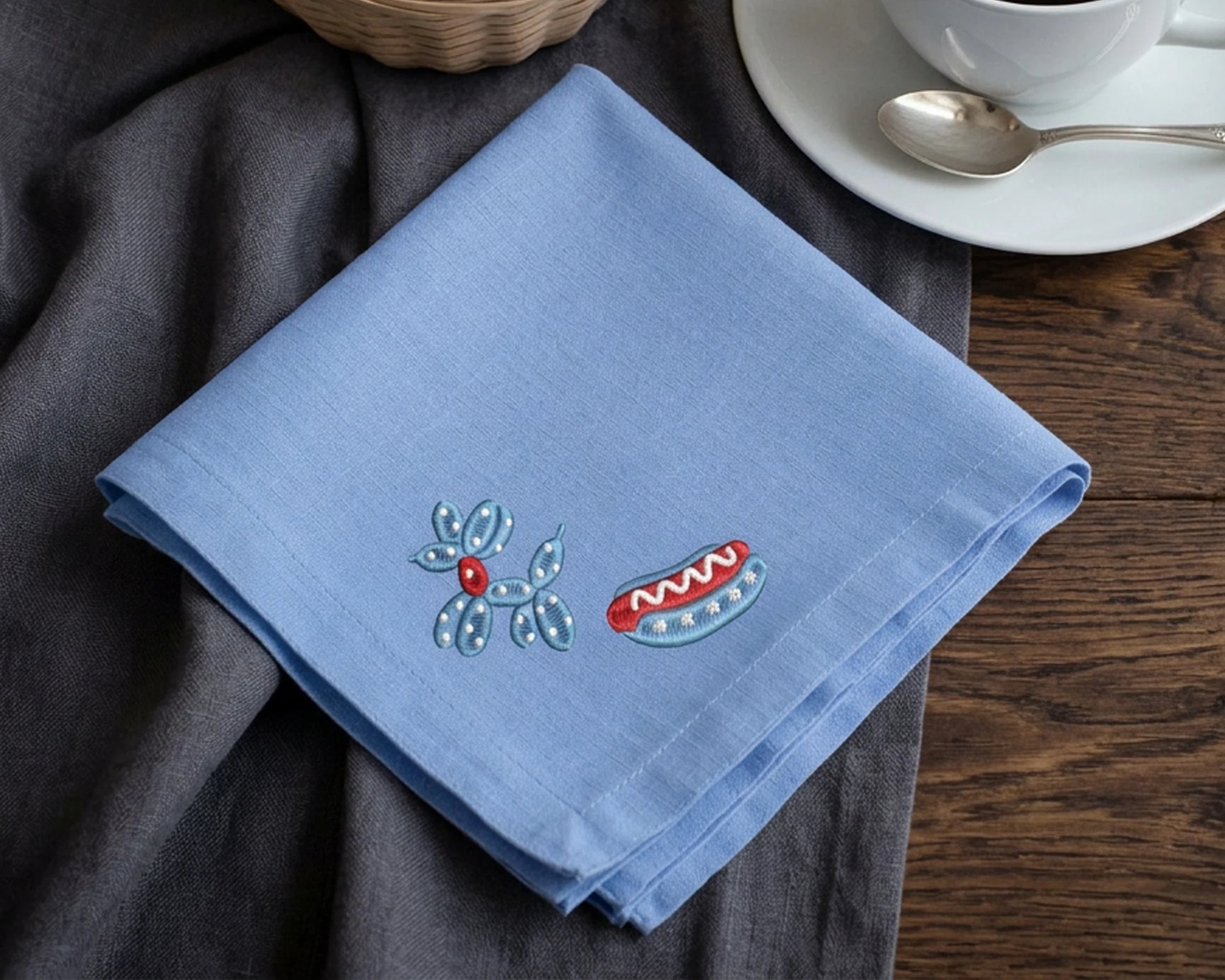 Blue hanky with embroidered designs on a wooden table with a cup and saucer.