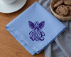 Blue napkin with purple angel design on a wooden table with cookies and a cup.