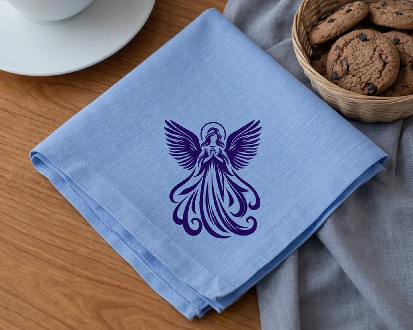 Blue napkin with purple angel design on a wooden table with cookies and a cup.