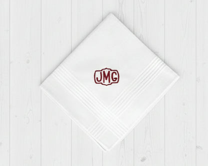 Single white cotton hanky for men with a burgundy embroidered crest monogram JMG on white wood