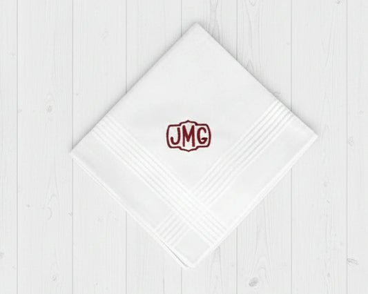 Single white cotton hanky for men with a burgundy embroidered crest monogram JMG on white wood