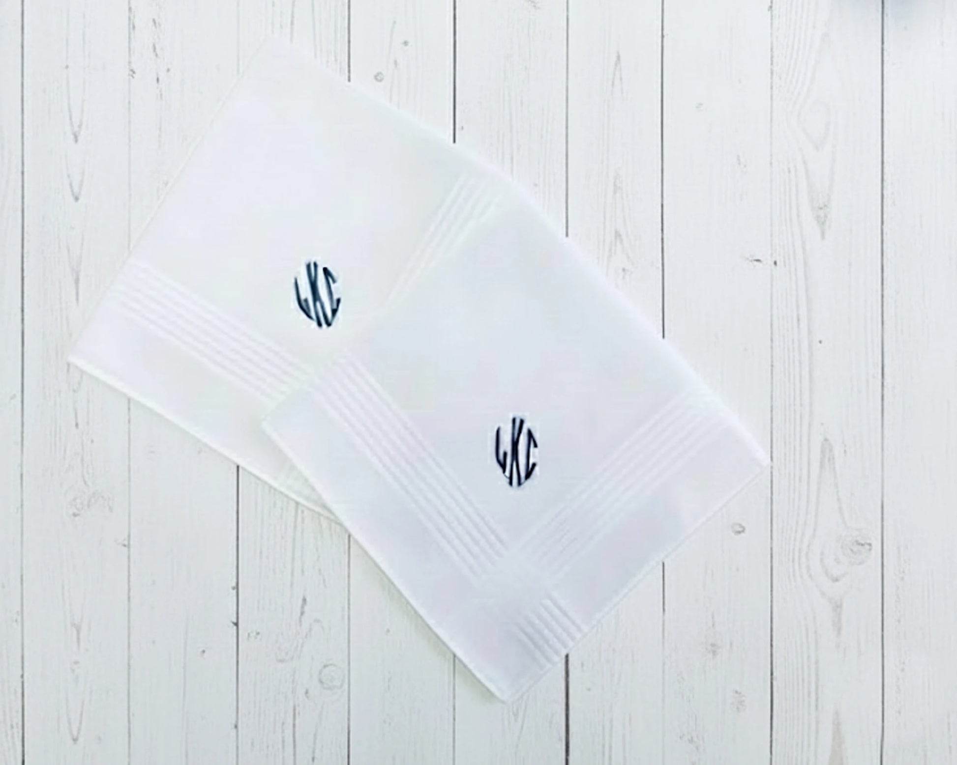 Single white cotton handkerchief with a copper-orange circular monogram PBR on a dark textured surface