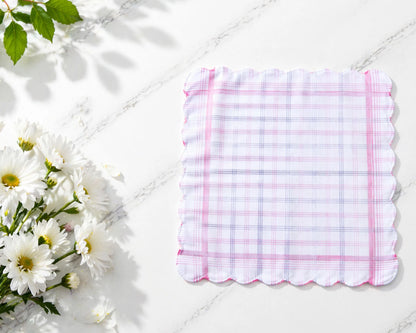 Checkered handkerchief with pink border on a white surface with flowers and leaves.