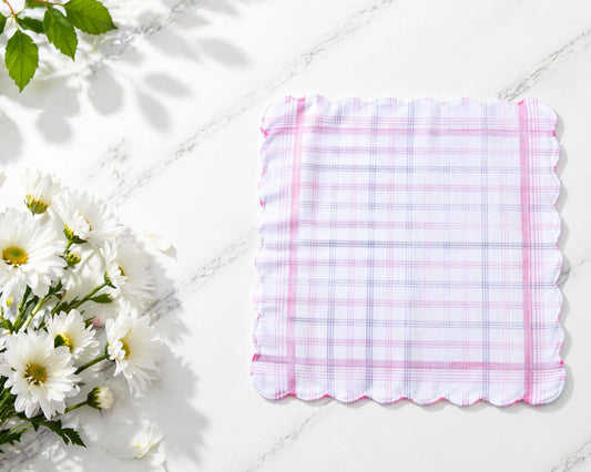 Checkered handkerchief with pink border on a white surface with flowers and leaves.