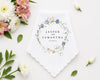 Checkered handkerchief with pink border on a white surface with flowers and leaves.
