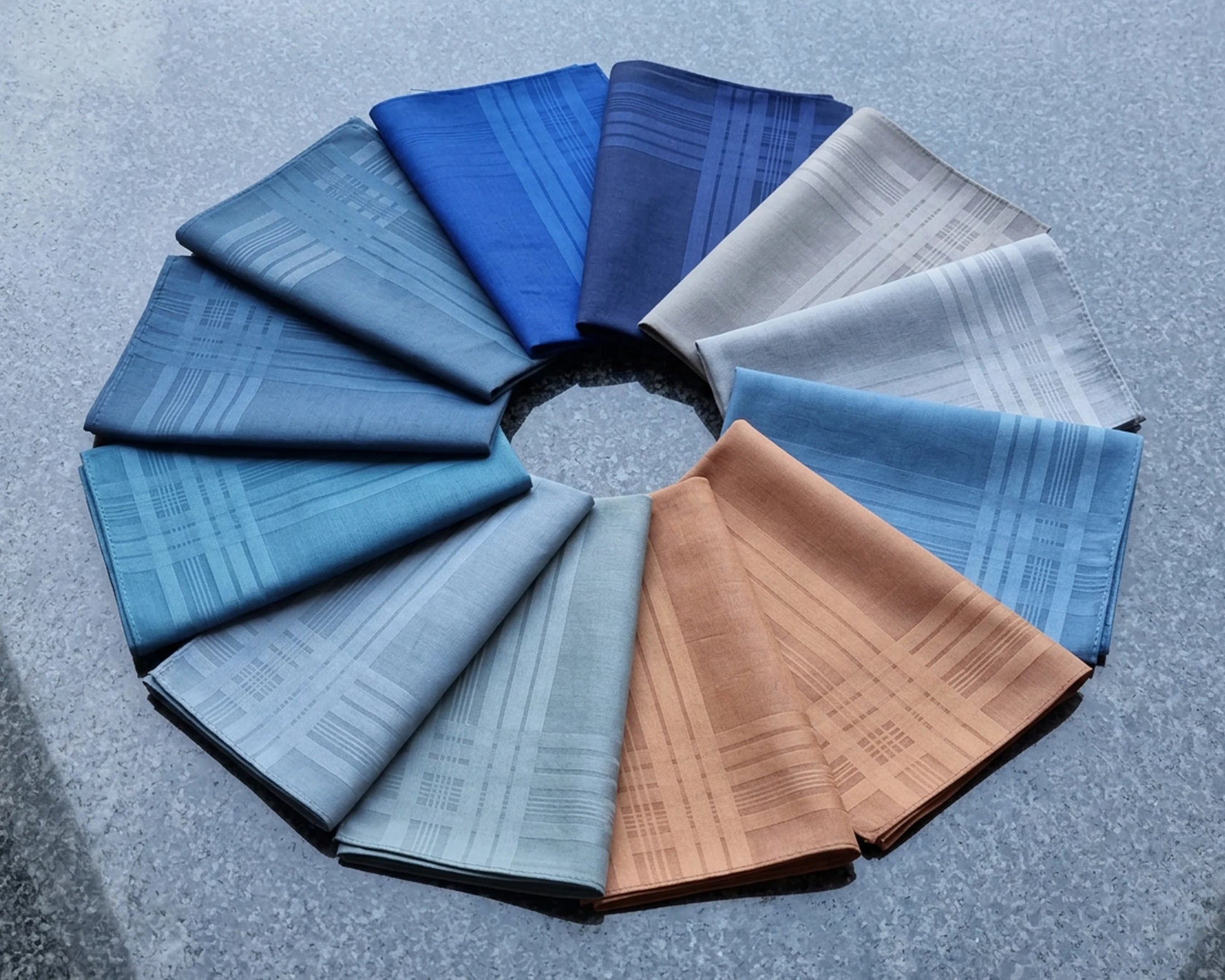 Circular arrangement of folded hanky  in various blue tones on a textured gray background