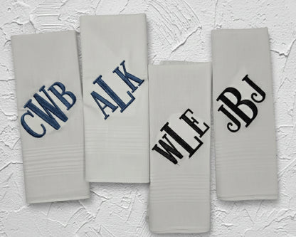 Four folded white cotton handkerchiefs showing diverse navy blue and black monogrammed initial embroidery