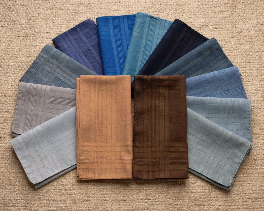 Collection of folded cotton hanky in various shades of blue and brown on a beige background