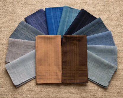Collection of folded cotton hanky in various shades of blue and brown on a beige background