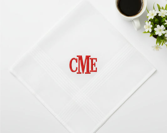 Single white cotton handkerchief with a bold red monogrammed CME initial near coffee and flowers