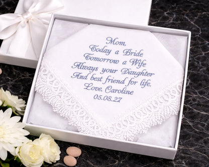 Embroidered handkerchief in a white box with personalized text on a dark surface with flowers.