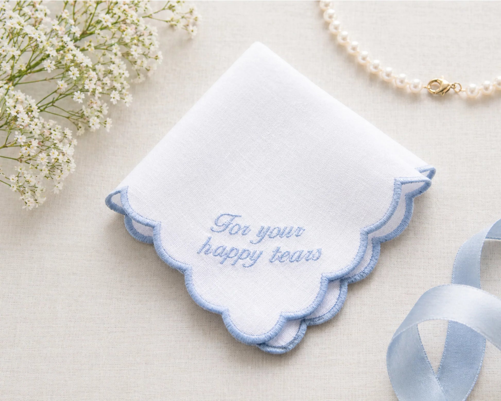 Embroidered handkerchief with 'For your happy tears' text on a light background with flowers and ribbon.
