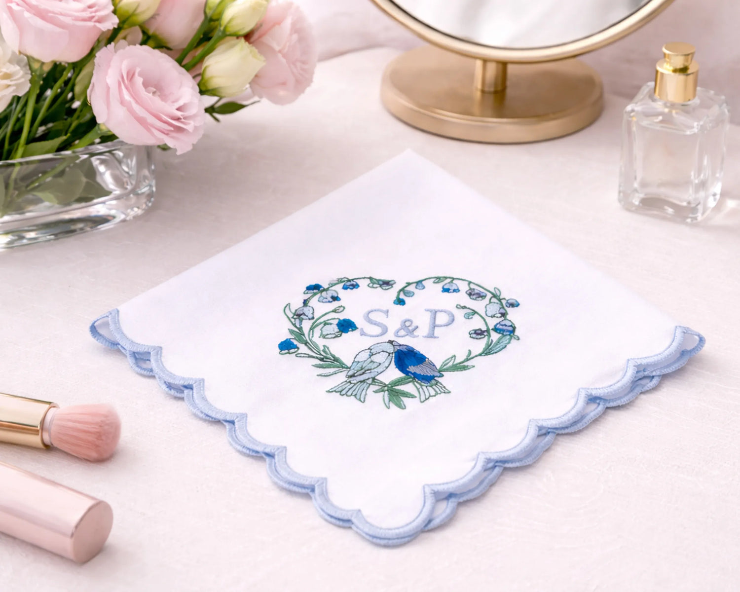 Embroidered handkerchief with 'S&P' design on a table with flowers and perfume.