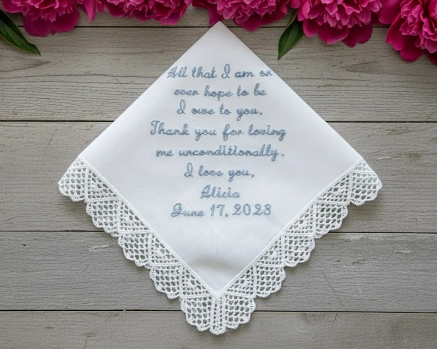 Embroidered handkerchief with personalized message on a wooden surface with pink flowers.