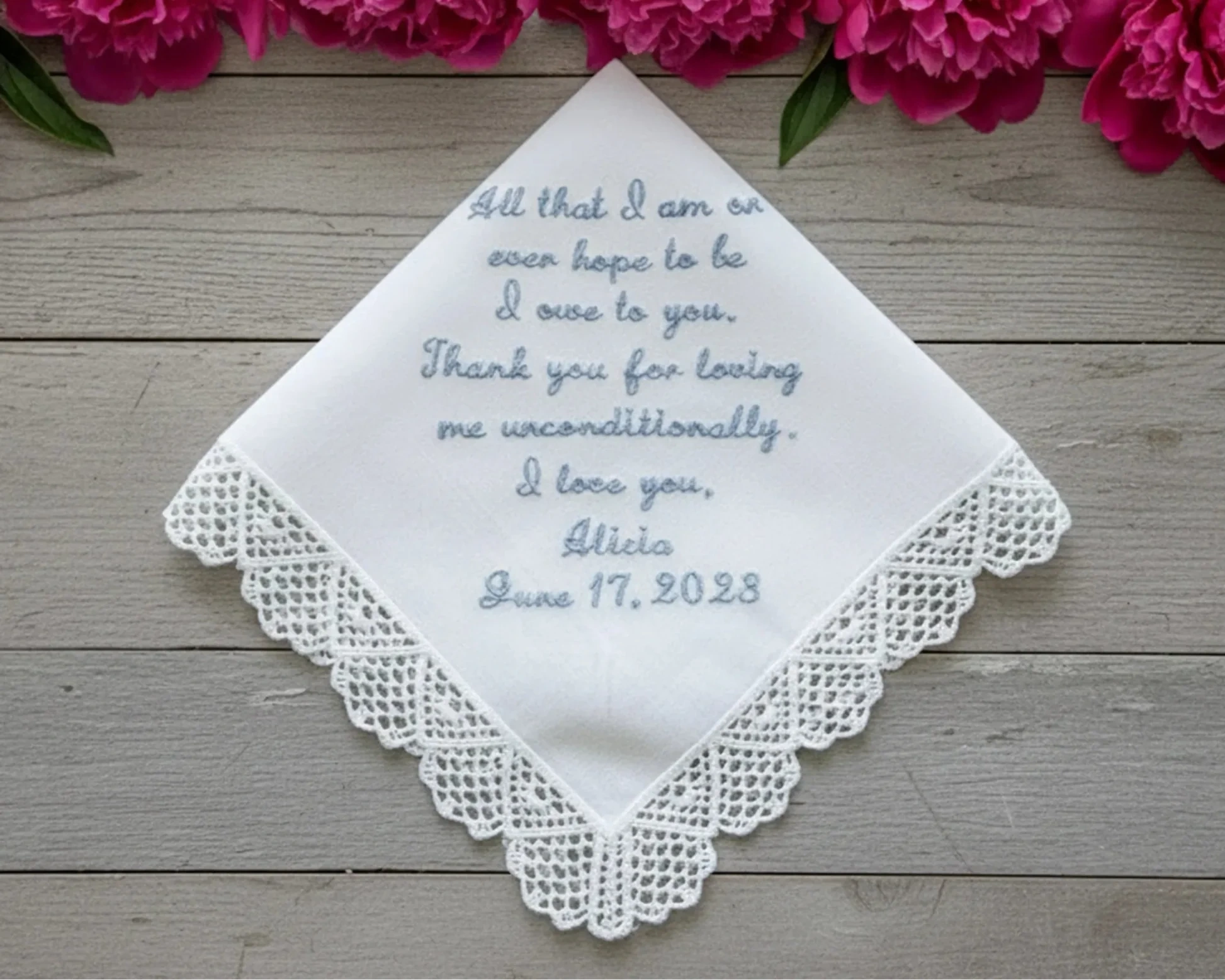 Embroidered handkerchief with personalized message on a wooden surface with pink flowers.