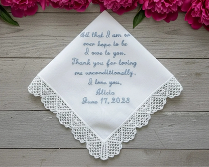 Embroidered handkerchief with personalized message on a wooden surface with pink flowers.